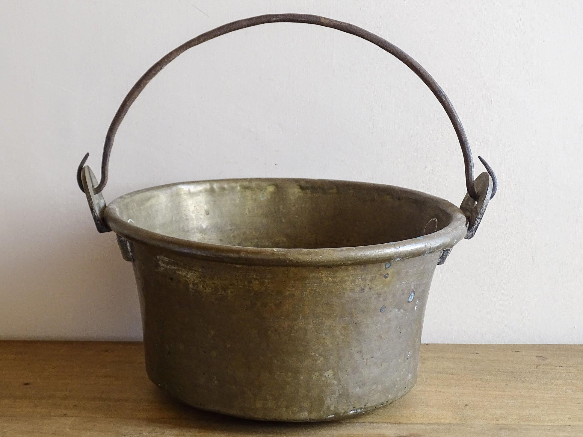 French antique brass cauldron with a hammered brass body and wrought iron handle, brass cooking pot ideal for farmhouse kitchen decor or rustic home decor, displayed on a wooden surface.