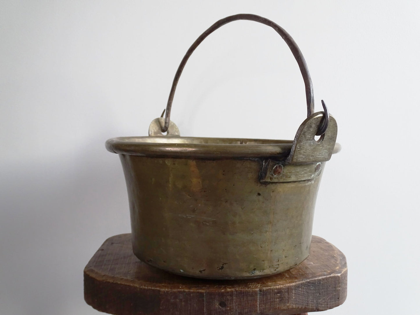 French antique brass cauldron with a hammered brass body and wrought iron handle, brass cooking pot ideal for farmhouse kitchen decor or rustic home decor, displayed on a wooden surface.