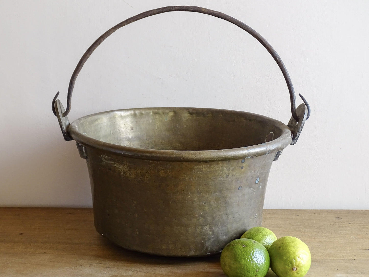 French antique brass cauldron with a hammered brass body and wrought iron handle, brass cooking pot ideal for farmhouse kitchen decor or rustic home decor, displayed on a wooden surface.