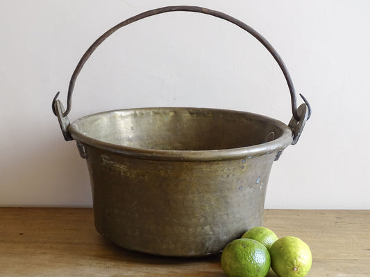 French antique brass cauldron with a hammered brass body and wrought iron handle, brass cooking pot ideal for farmhouse kitchen decor or rustic home decor, displayed on a wooden surface.