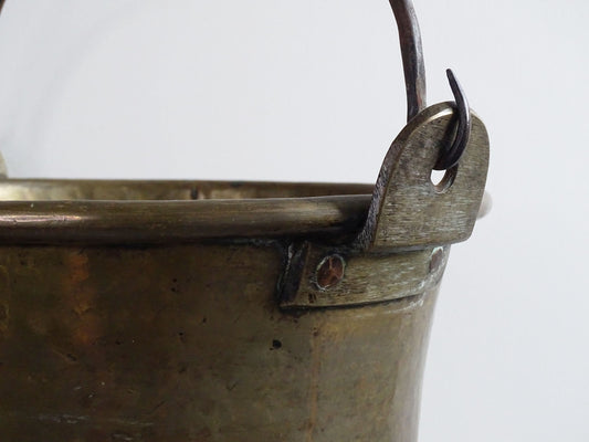 French antique brass cauldron with a hammered brass body and wrought iron handle, brass cooking pot ideal for farmhouse kitchen decor or rustic home decor, displayed on a wooden surface.