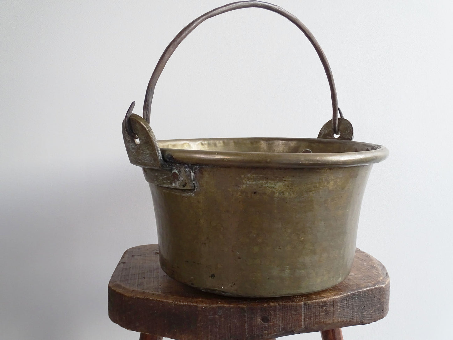 French antique brass cauldron with a hammered brass body and wrought iron handle, brass cooking pot ideal for farmhouse kitchen decor or rustic home decor, displayed on a wooden surface.