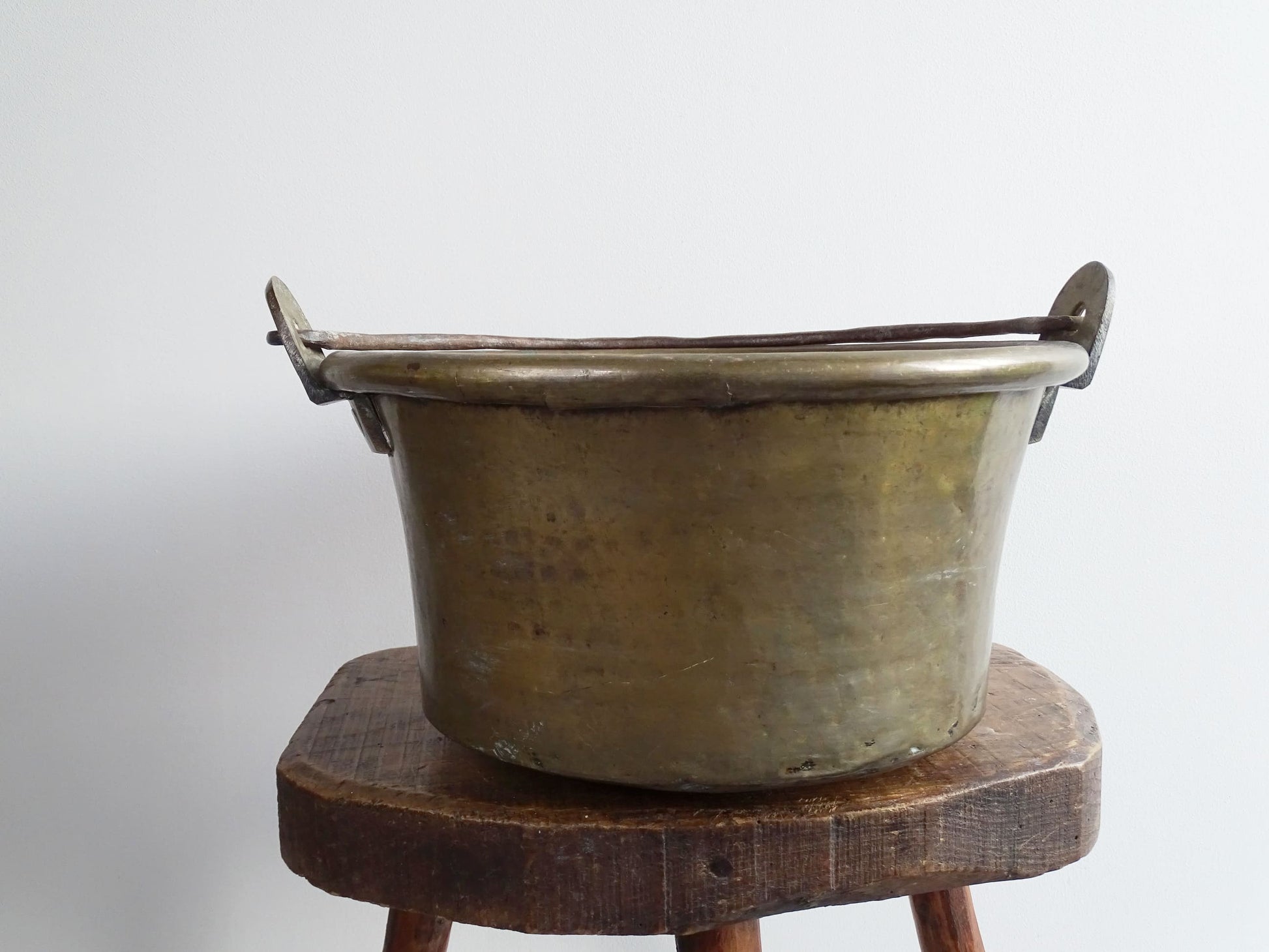 French antique brass cauldron with a hammered brass body and wrought iron handle, brass cooking pot ideal for farmhouse kitchen decor or rustic home decor, displayed on a wooden surface.