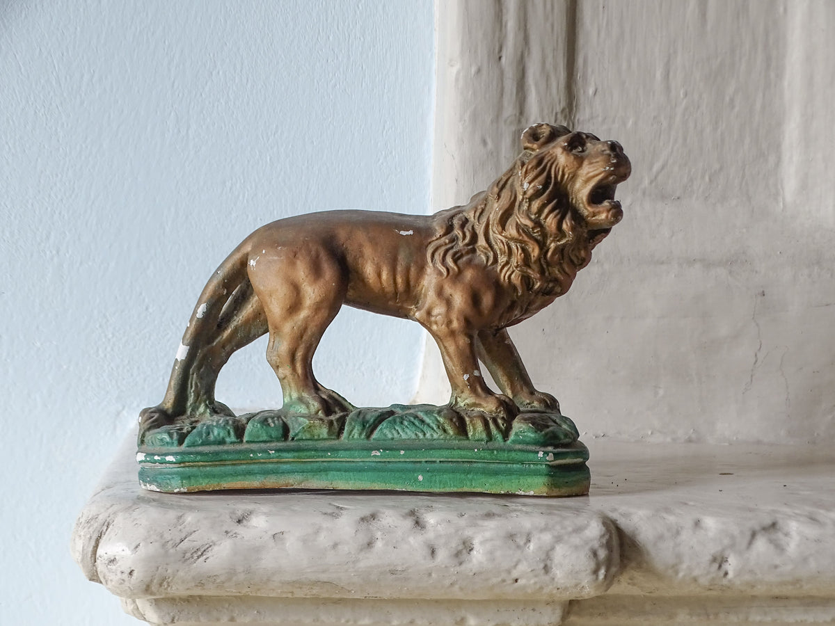French vintage lion in plaster, painted in gold and green. Pictured on a country house fireplace