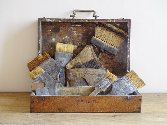 French antique paint box filled with paint brushes and painter’s tools. It has specks of paint and the outside of the wooden box has a “D” initial. The artist's box or painter's box has a rich patina.