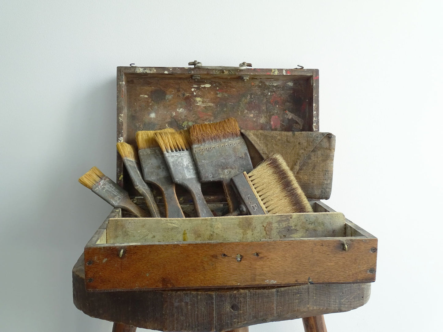 French antique paint box filled with paint brushes and painter’s tools. It has specks of paint and the outside of the wooden box has a “D” initial. The artist's box or painter's box has a rich patina.