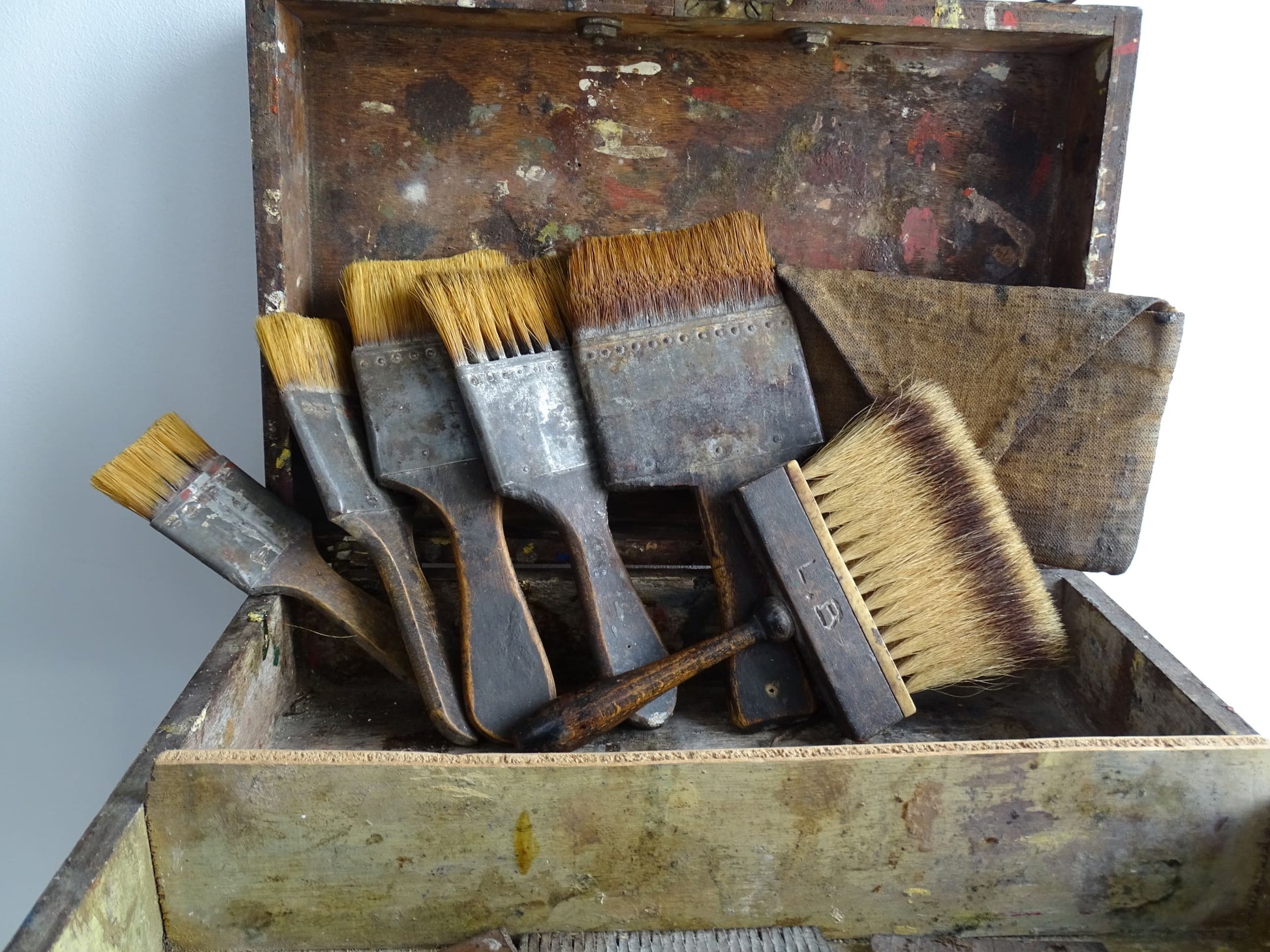 French antique paint box filled with paint brushes and painter’s tools. It has specks of paint and the outside of the wooden box has a “D” initial. The artist's box or painter's box has a rich patina.