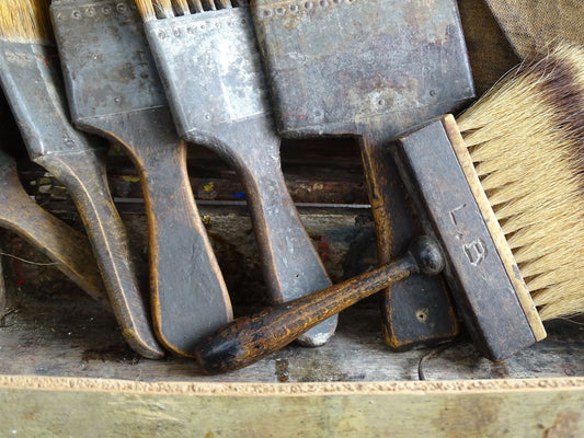 French antique paint box filled with paint brushes and painter’s tools. It has specks of paint and the outside of the wooden box has a “D” initial. The artist's box or painter's box has a rich patina.