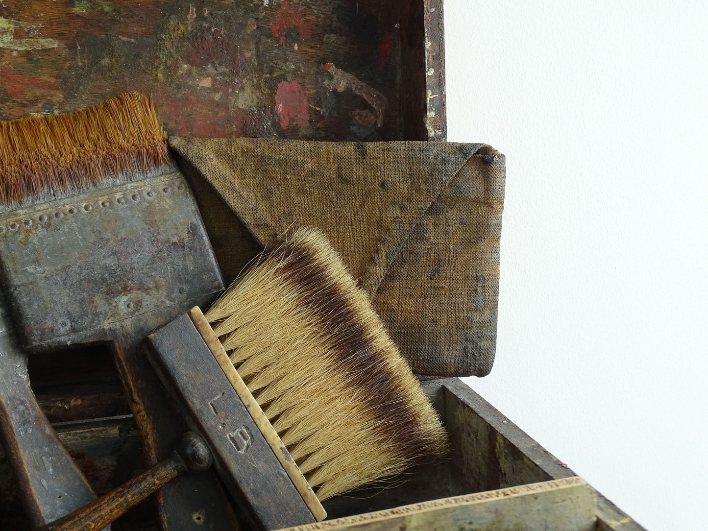 French antique paint box filled with paint brushes and painter’s tools. It has specks of paint and the outside of the wooden box has a “D” initial. The artist's box or painter's box has a rich patina.