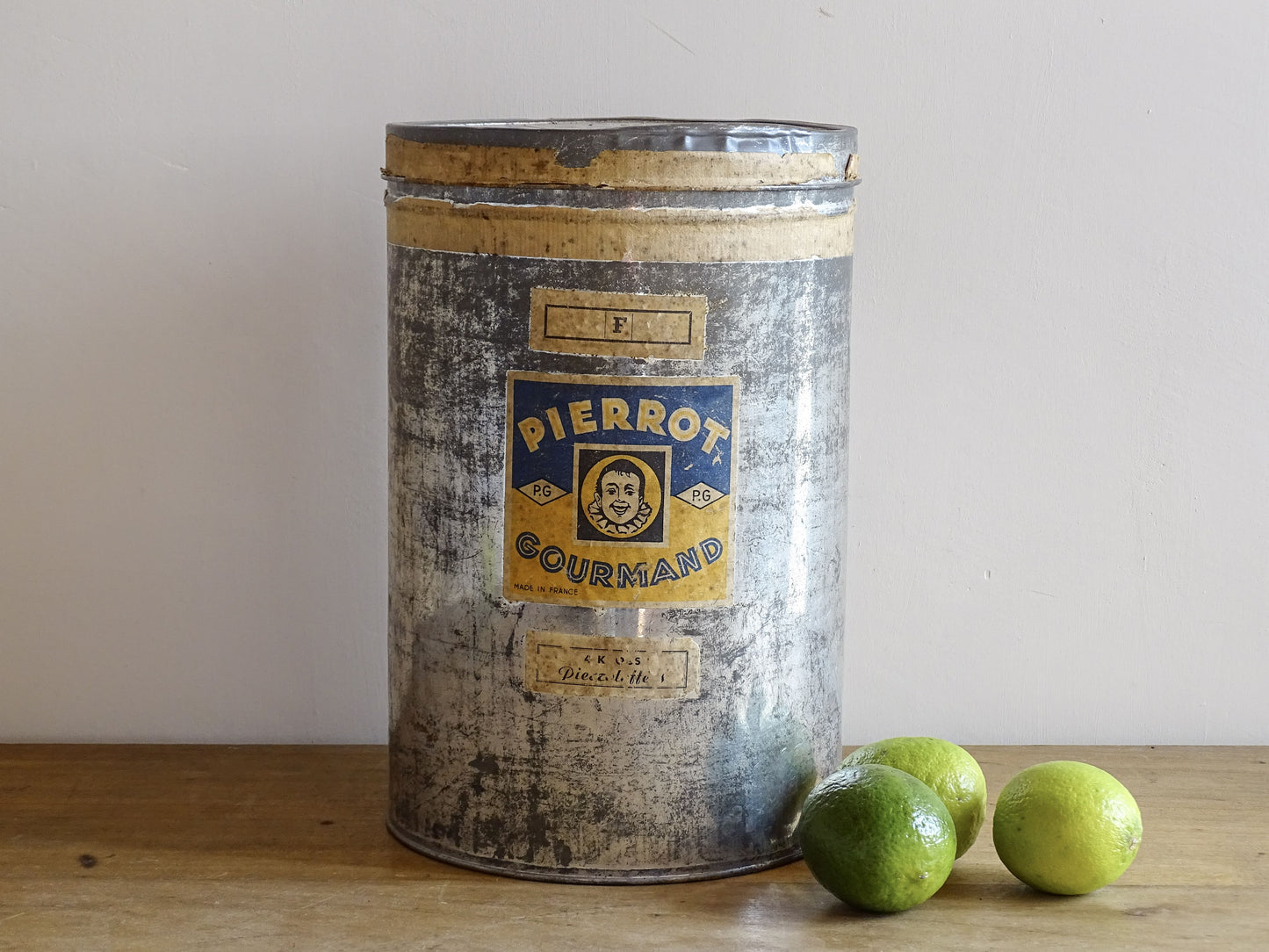 Vintage metal canister with 'Pierrot Gourmand' label on a wooden surface with limes.