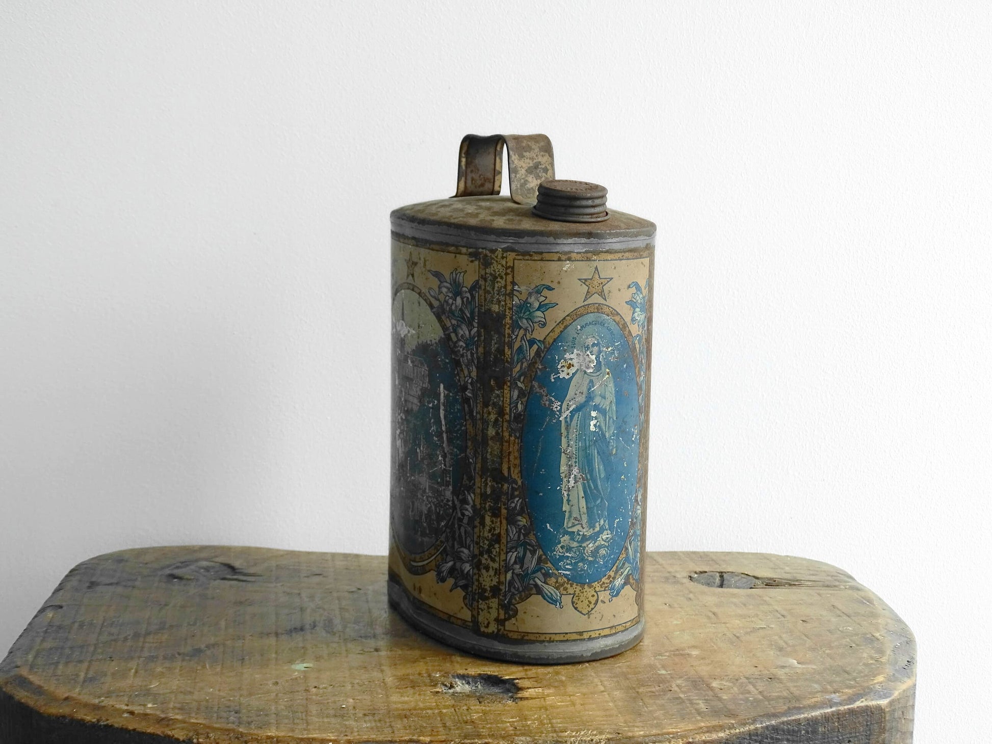 French antique Lourdes souvenir water flask. Pewter tin where the top is decorated with fleur de lis, one side depicts the cathedral (Sanctuaire de Notre-Dame de Lourdes), the other shows a crowd of people. To the side is the Virgin Mary, above her it says “Je suis l'Immaculée Conception”. The antique flask for religious decor.