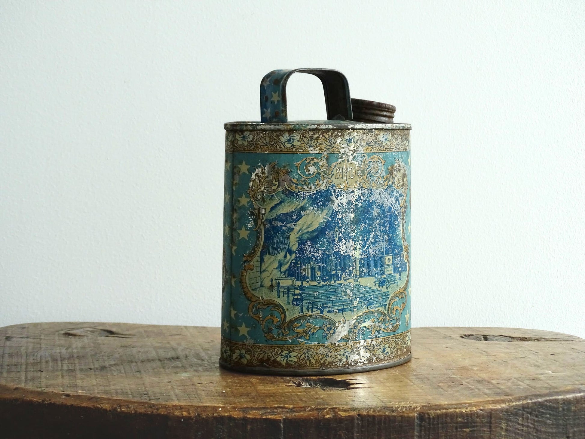 French antique Lourdes souvenir water flask in light blue, made from pewter, the top is decorated with stars, one side shows a view towards the cathedral (Sanctuaire de Notre-Dame de Lourdes), the other shows pilgrims in early 20th century dress attending mass at the Grotto of Massabielle. To the side is a depiction of the Virgin Mary. Flask for Lourdes holy water. Antique Lourdes souvenir religious decor.