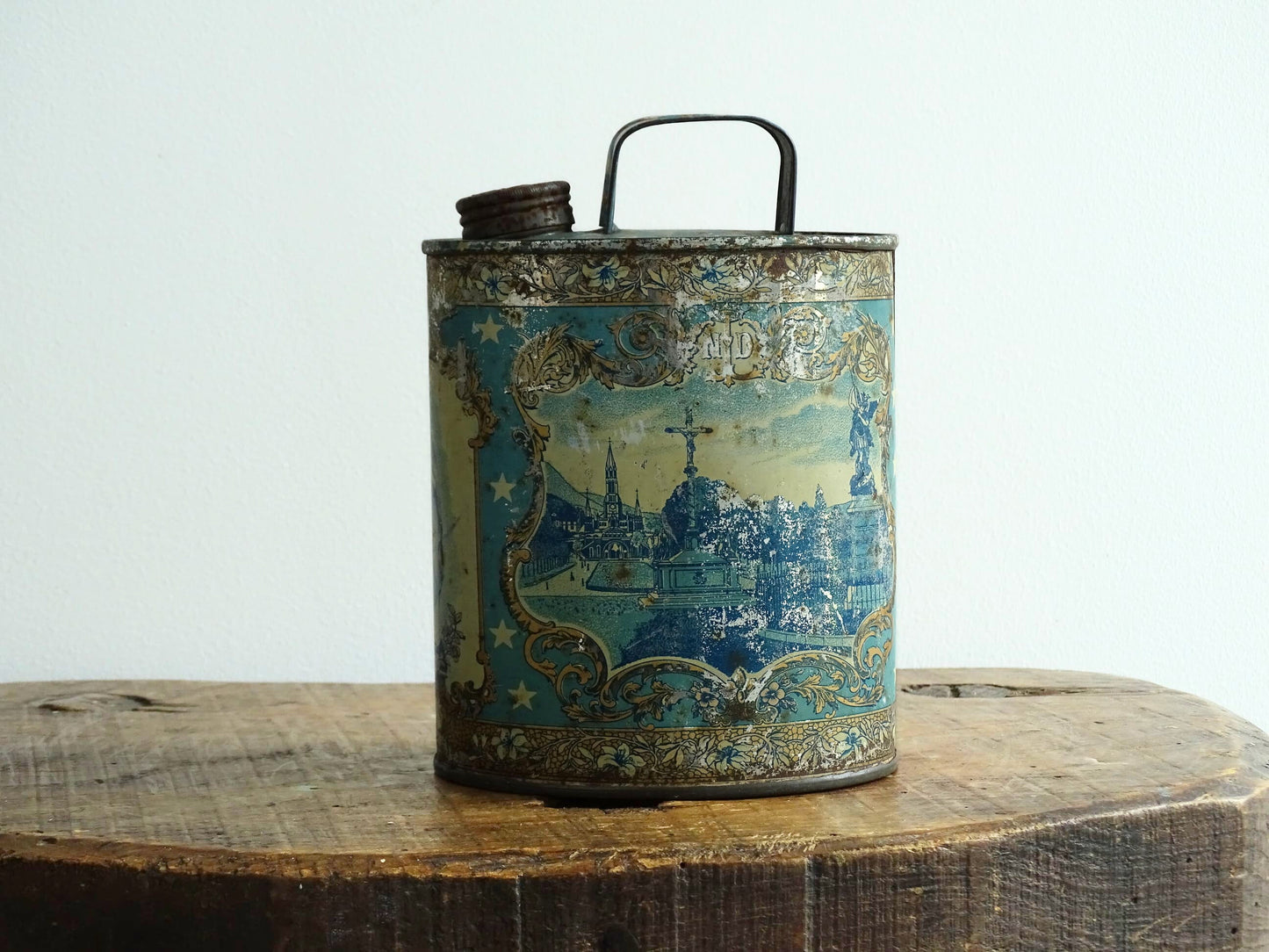 French antique Lourdes souvenir water flask in light blue, made from pewter, the top is decorated with stars, one side shows a view towards the cathedral (Sanctuaire de Notre-Dame de Lourdes), the other shows pilgrims in early 20th century dress attending mass at the Grotto of Massabielle. To the side is a depiction of the Virgin Mary. Flask for Lourdes holy water. Antique Lourdes souvenir religious decor.