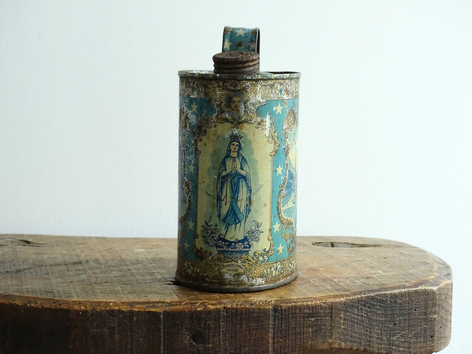 French antique Lourdes souvenir water flask in light blue, made from pewter, the top is decorated with stars, one side shows a view towards the cathedral (Sanctuaire de Notre-Dame de Lourdes), the other shows pilgrims in early 20th century dress attending mass at the Grotto of Massabielle. To the side is a depiction of the Virgin Mary. Flask for Lourdes holy water. Antique Lourdes souvenir religious decor.