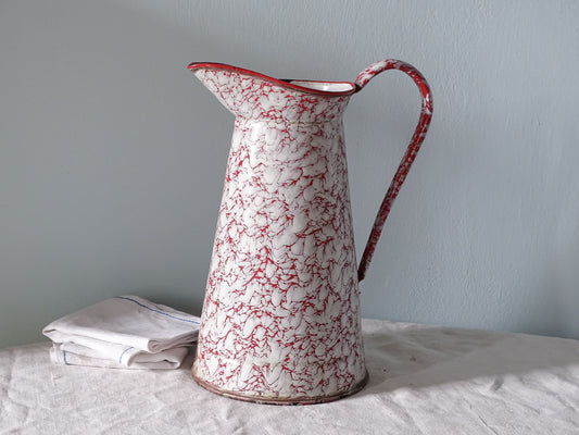 French vintage enamelware pitcher with red marble effect, pictured with antique linen in front of a pale blue wall