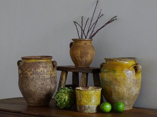 Antique French confit pots with yellow glaze alongside wood with patina and textured pottery.