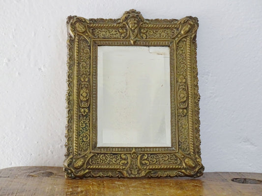 Small French antique brass mirror. The frame is embossed and decorated with a face, flowers and scroll design. Antique French mirror or Foxed mirror.