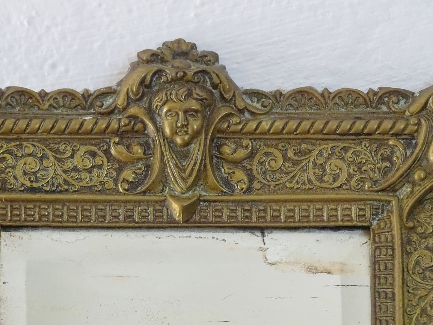 Small French antique brass mirror. The frame is embossed and decorated with a face, flowers and scroll design. Antique French mirror or Foxed mirror.