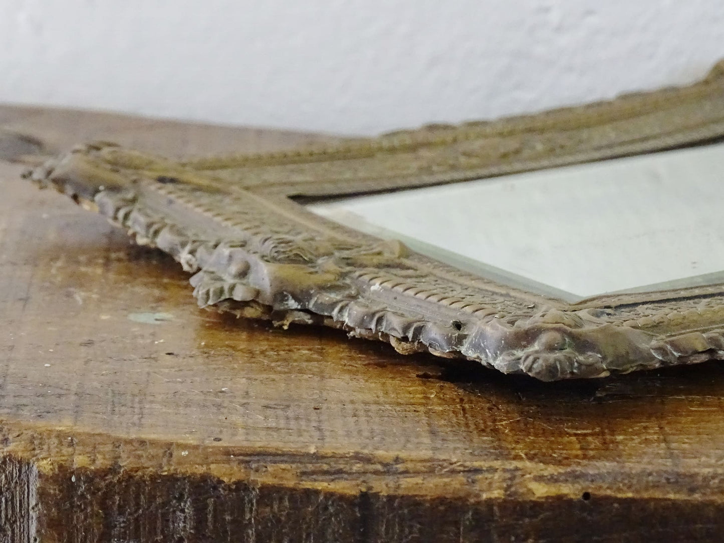 Small French antique brass mirror. The frame is embossed and decorated with a face, flowers and scroll design. Antique French mirror or Foxed mirror.