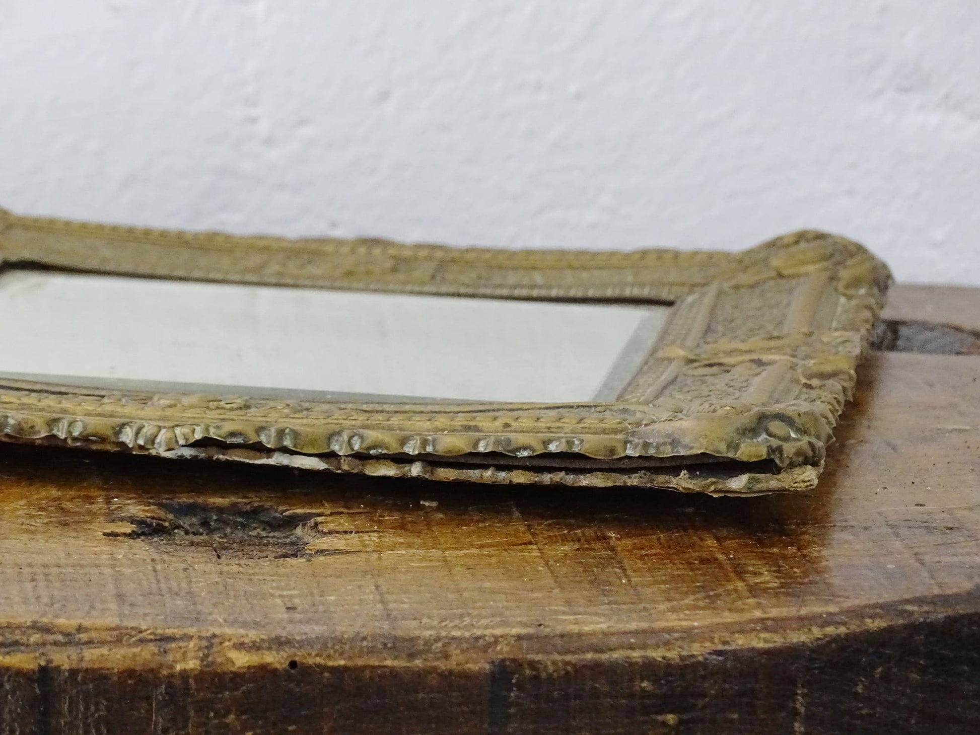 Small French antique brass mirror. The frame is embossed and decorated with a face, flowers and scroll design. Antique French mirror or Foxed mirror.