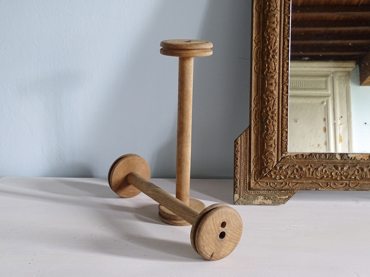 Two vintage wooden bobbins, pictured with a gold mirror
