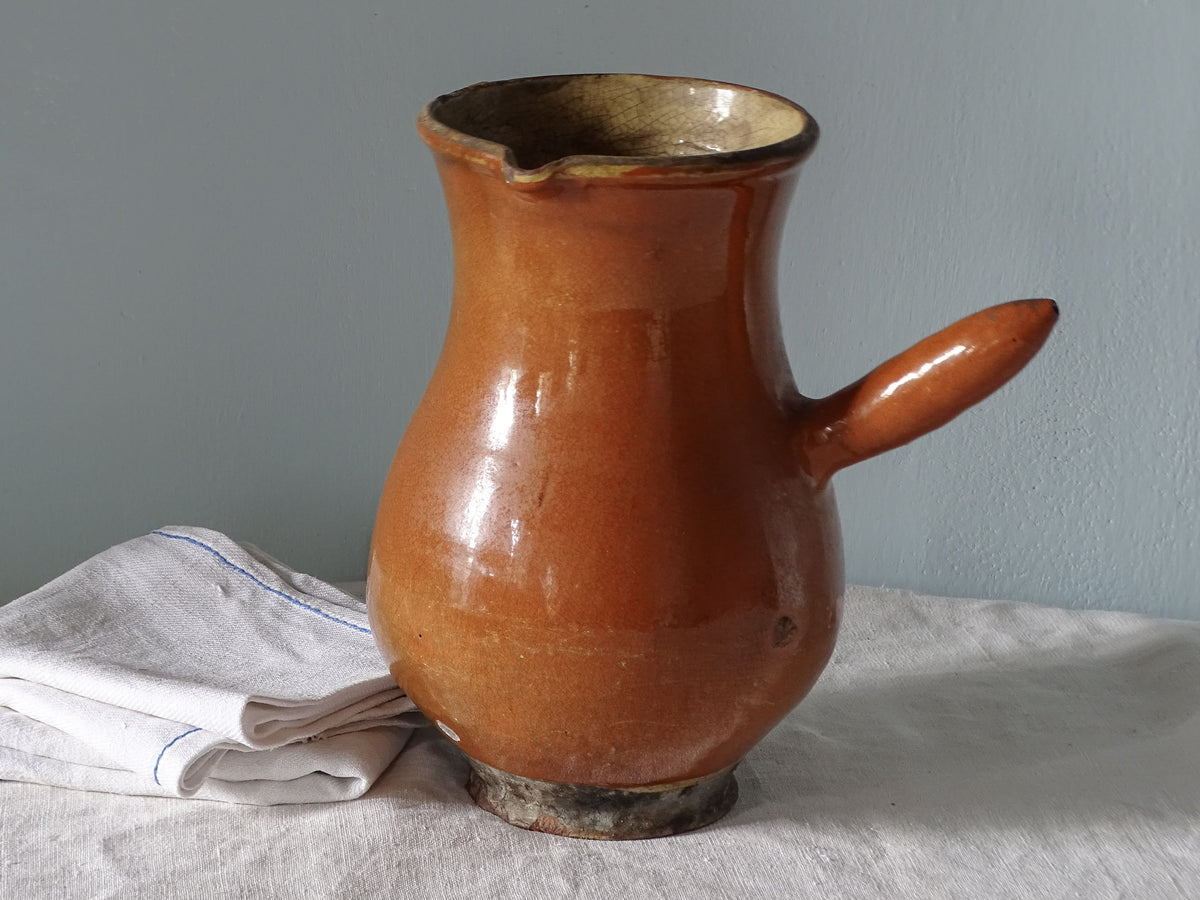 French antique ceramic pitcher with red glazed exterior and yellow glaze interior. Pictured with antique linen