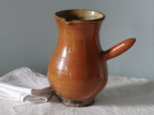French antique ceramic pitcher with red glazed exterior and yellow glaze interior. Pictured with antique linen