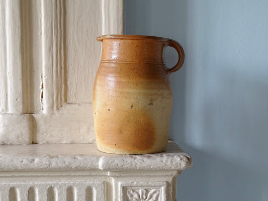French antique pottery pitcher with a brown glaze, pictured on a carved stone fireplace in a country house