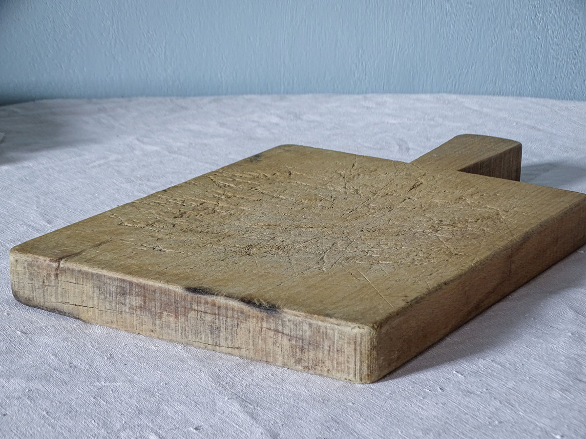 Angled view of vintage French wooden cutting board showing its thick edges, rectangular shape and heavily knife-marked surface.