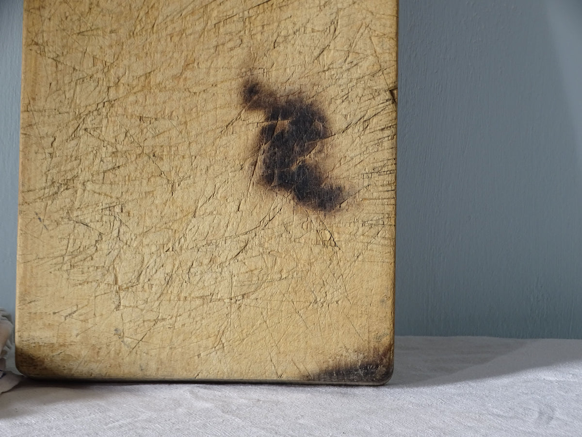 Close-up of vintage French wooden cutting board showing an old dark scorch mark and numerous knife marks across the surface.