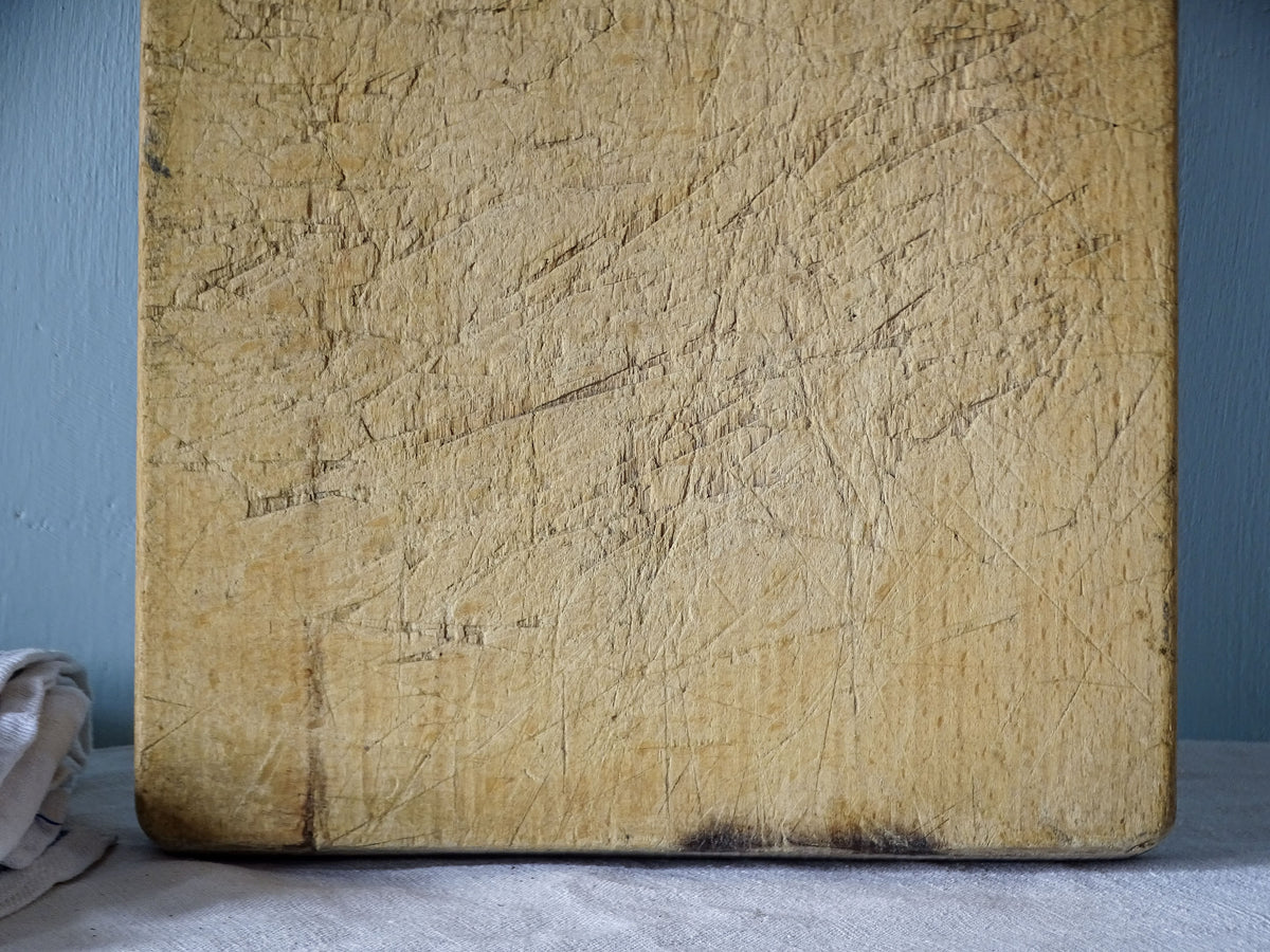 Detail of vintage French chopping board showing overlapping knife marks, worn edges and darker areas of aged wood.