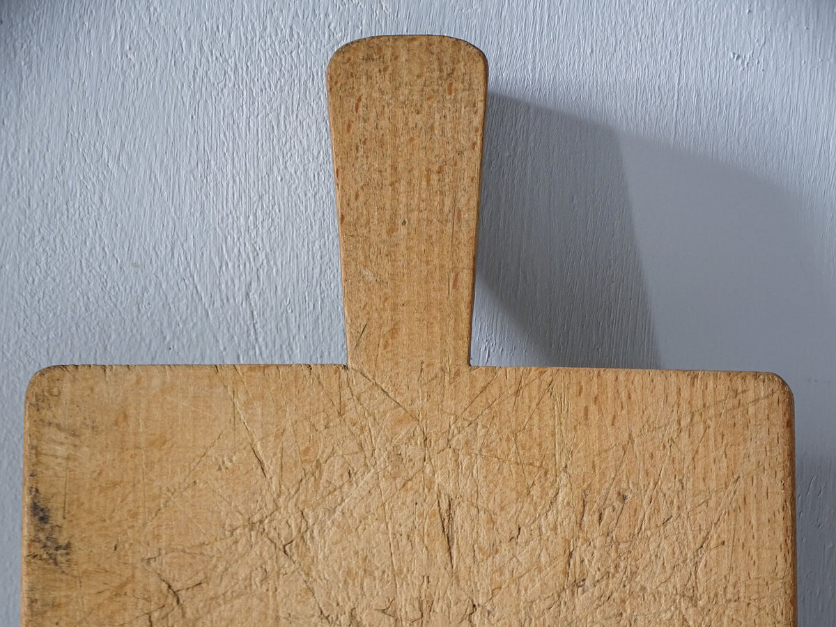 Close-up of long, slightly flared handle on vintage French wooden cutting board, showing its rounded end and worn surface.