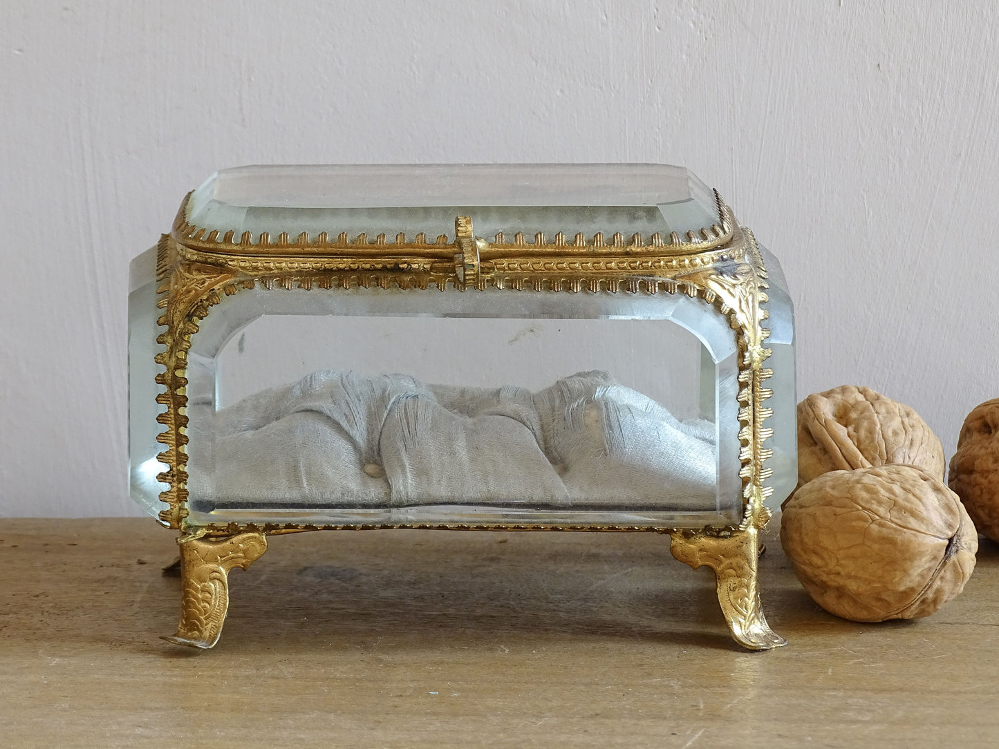 French antique glass jewelry box with bevelled glass. Antique trinket box with a pale blue silk covered cushion. Decorative gilt metal surrounds the thick, bevelled glass panels.