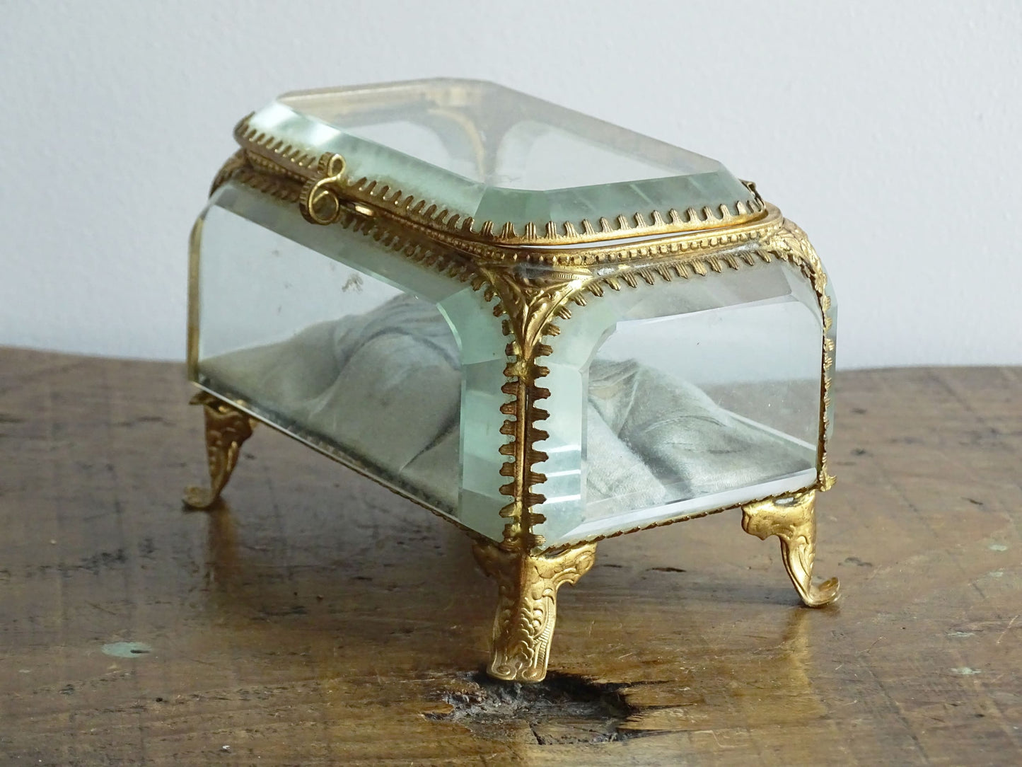 French antique glass jewelry box with bevelled glass. Antique trinket box with a pale blue silk covered cushion. Decorative gilt metal surrounds the thick, bevelled glass panels.