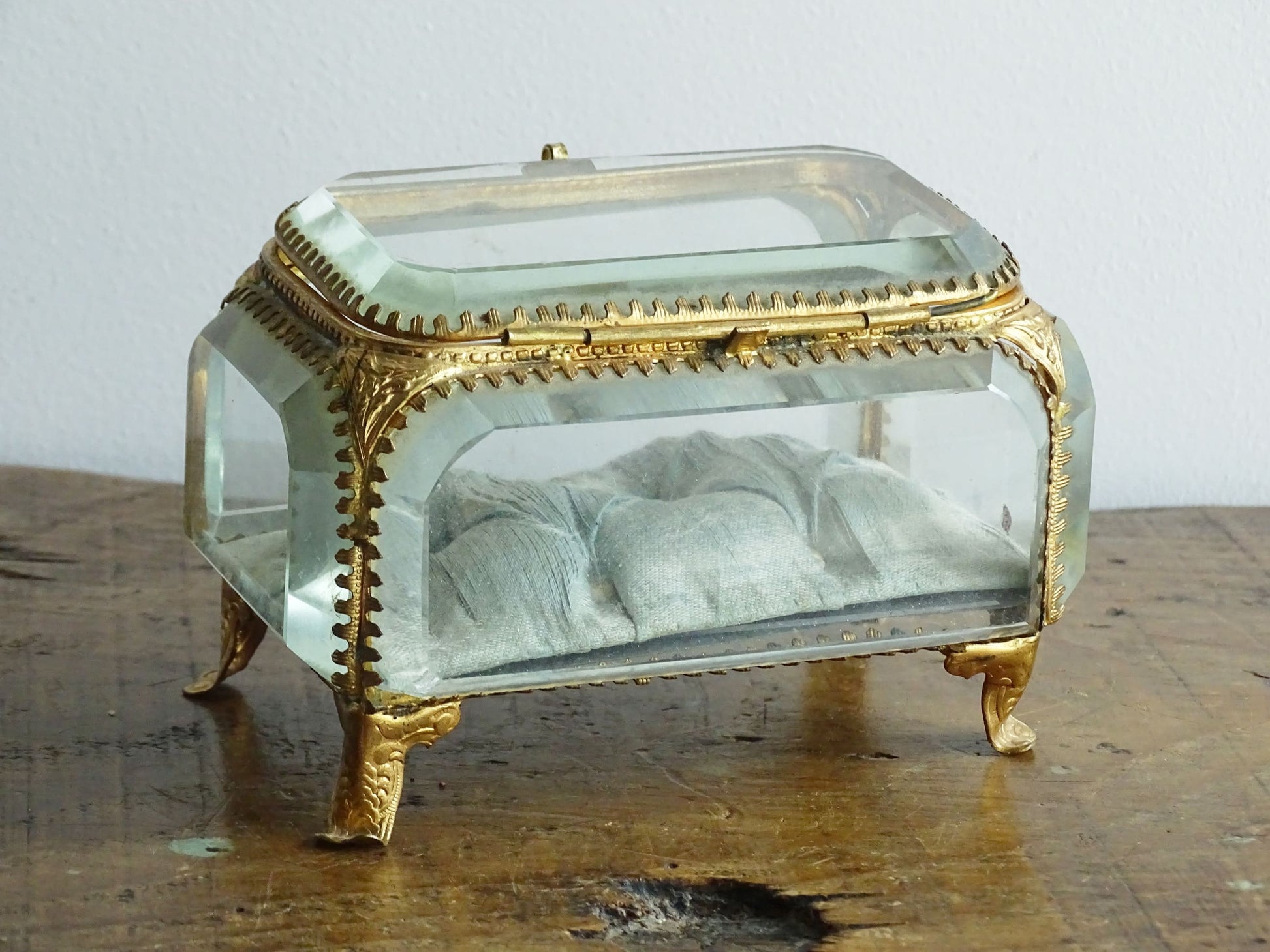 French antique glass jewelry box with bevelled glass. Antique trinket box with a pale blue silk covered cushion. Decorative gilt metal surrounds the thick, bevelled glass panels.