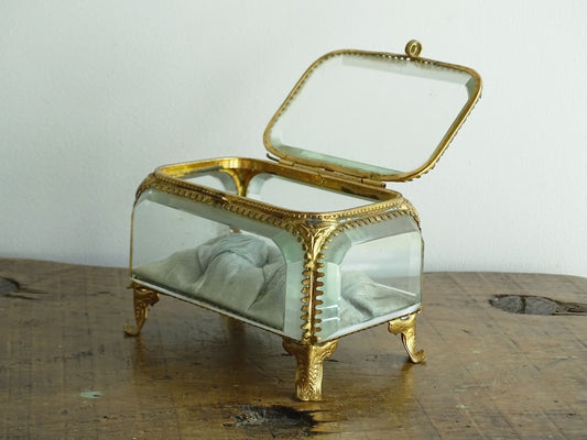 French antique glass jewelry box with bevelled glass. Antique trinket box with a pale blue silk covered cushion. Decorative gilt metal surrounds the thick, bevelled glass panels.