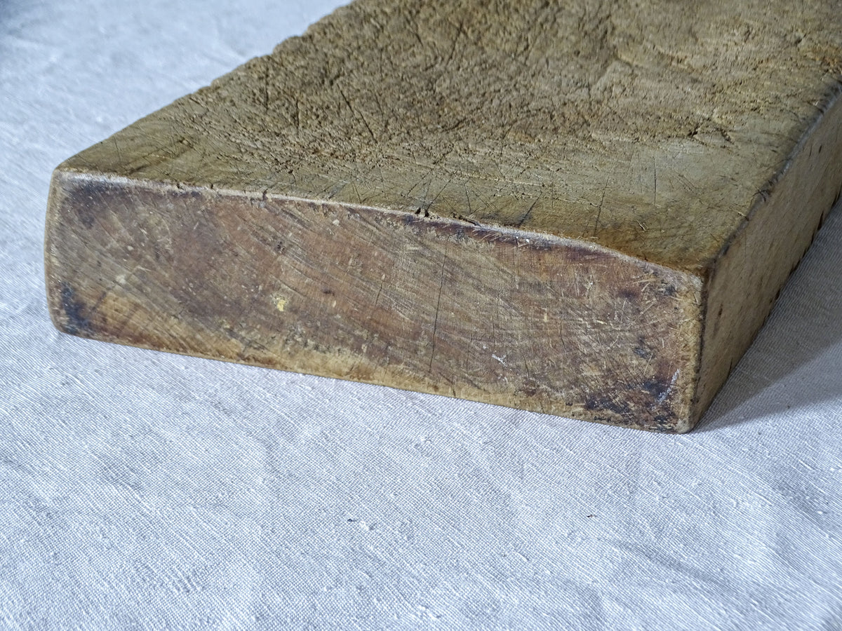 Close-up of antique French wooden cutting board showing its substantial thickness, heavily worn surface and darkened edges.