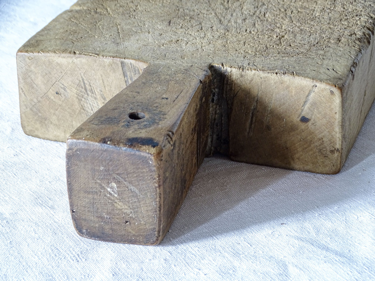Detail of thick antique French chopping board showing its integral wooden handle, hanging hole and aged patina.