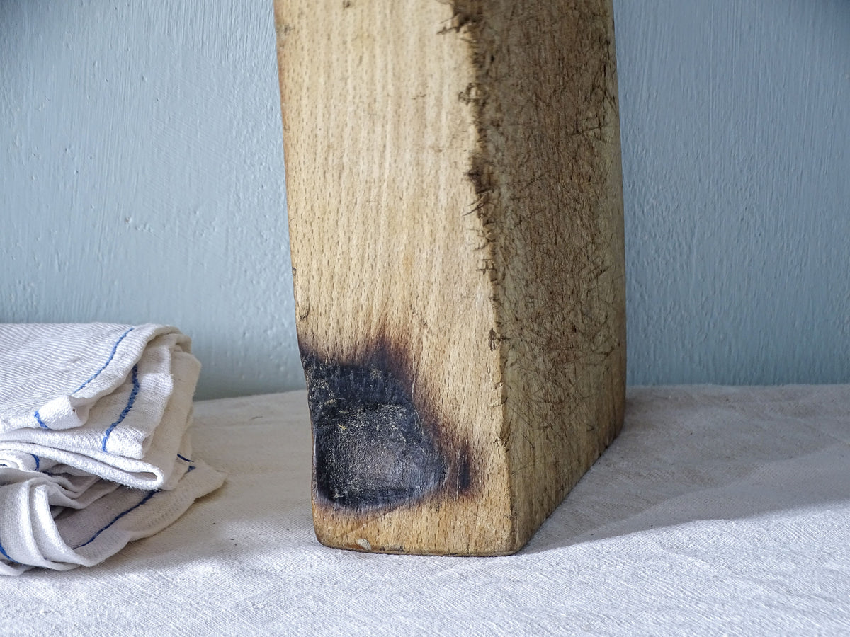 Detail of antique French chopping board showing a darkened patch on the edge of its thick solid wood construction.