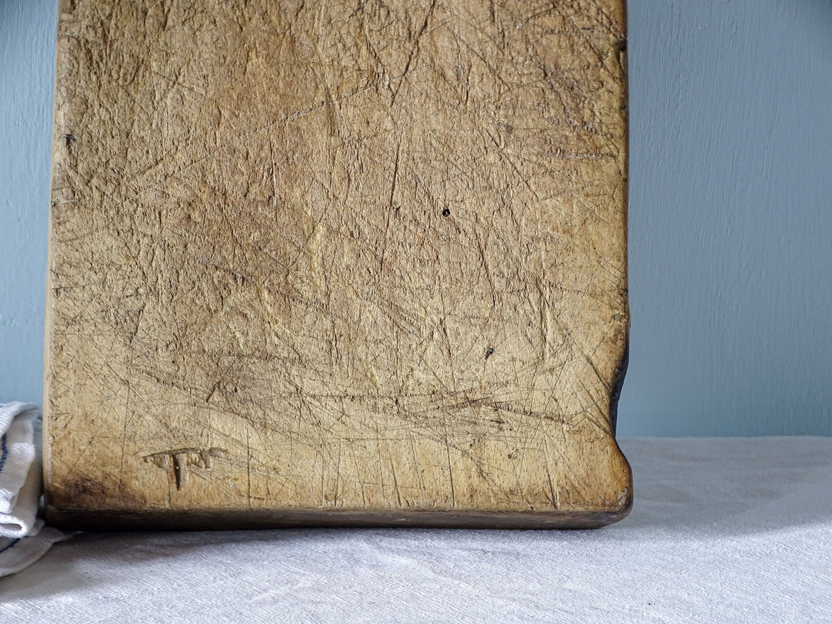 Close-up of heavily worn antique wooden cutting board surface covered with numerous deep knife marks and scratches.