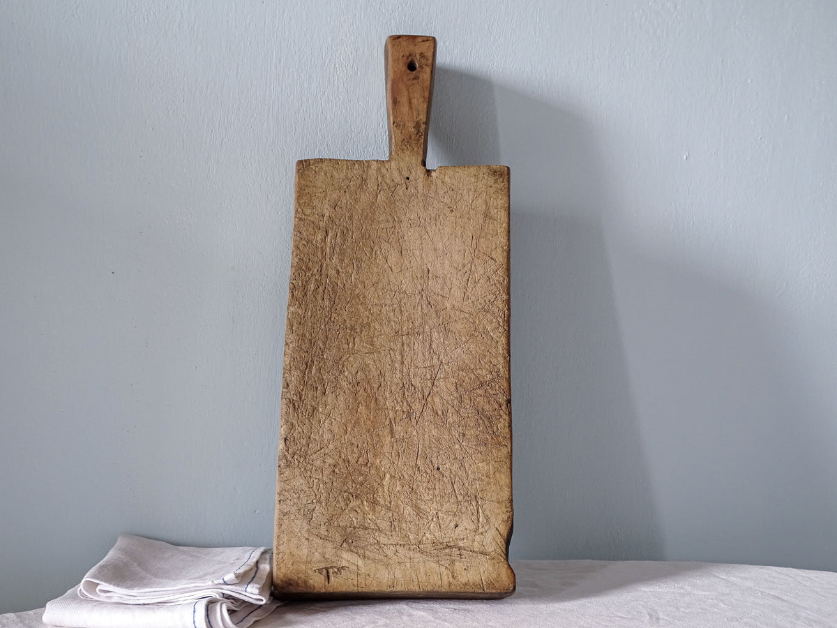 Antique French wooden chopping board with long rectangular shape, short handle and heavily worn cutting surface.