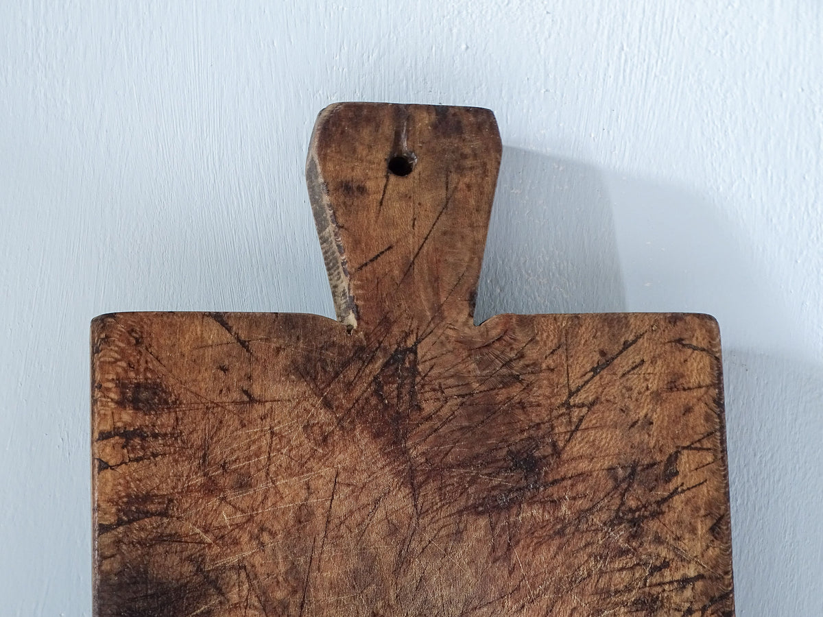 Close-up of the short tapered handle and hanging hole on a French antique wooden cutting board, showing scratches and aged wood.