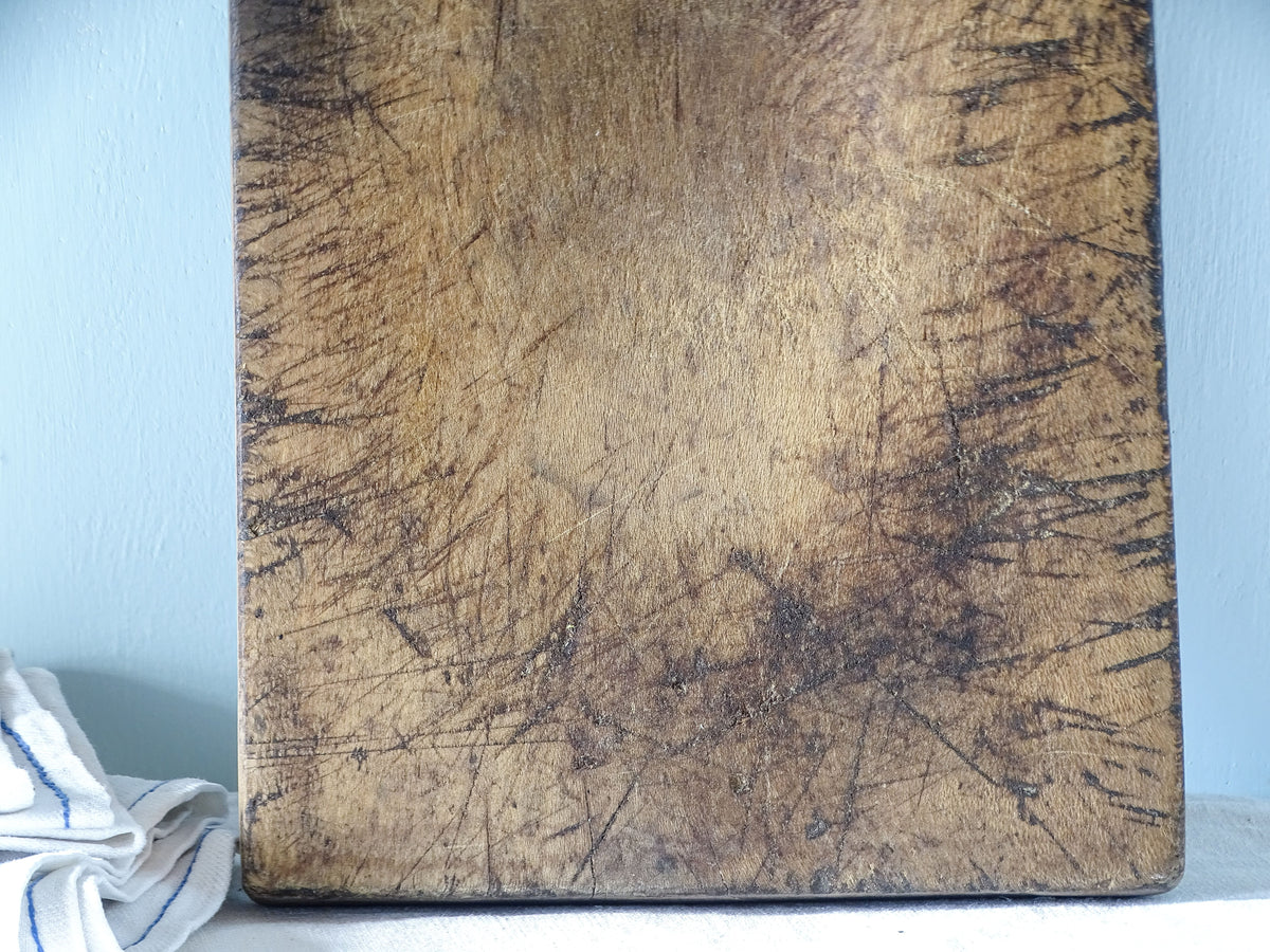 Detailed view of the heavily worn surface of an antique wooden chopping board with old knife marks, darkened edges and warm brown patina.