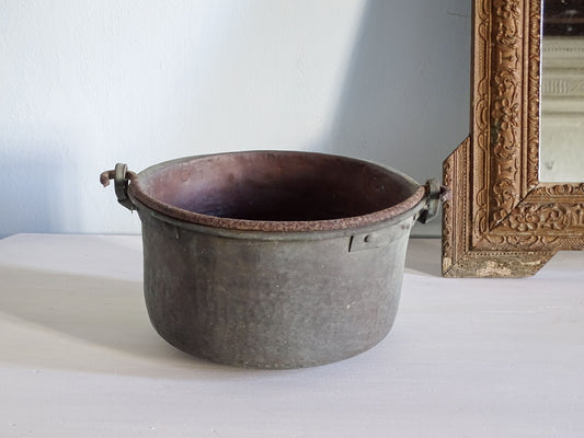Worn French antique copper cauldron with verdigris, pictured on a white table next to a gold mirror in front of a light blue wall