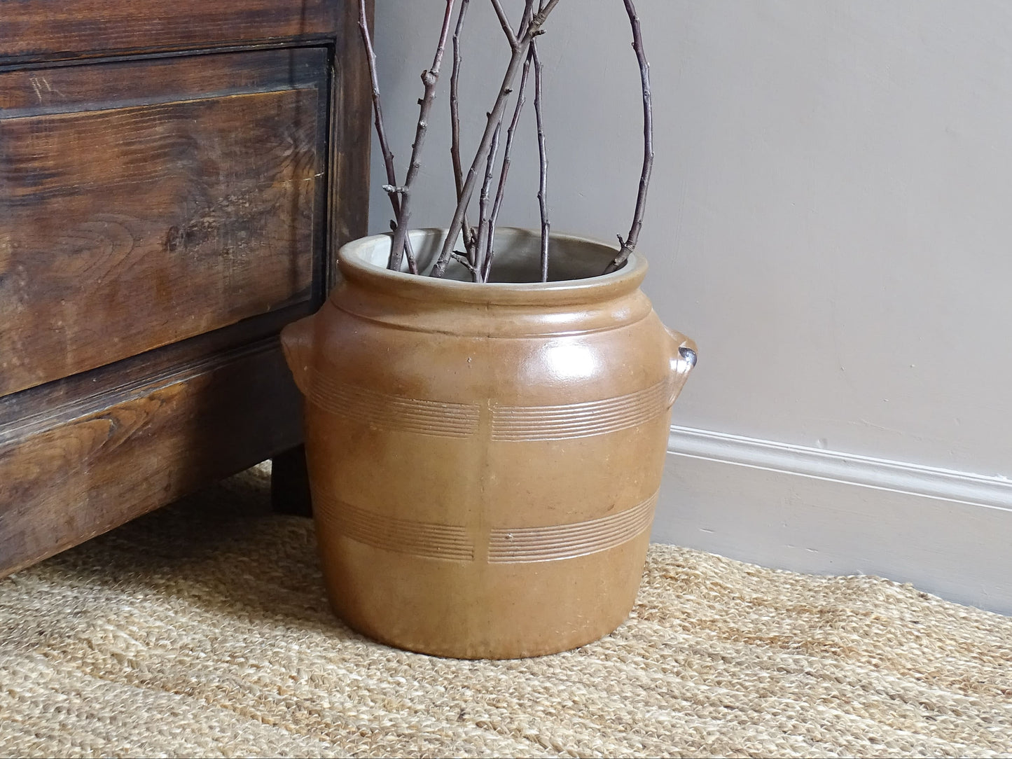 French antique stoneware cache pot or confit jar with a brown glaze, filled with branches.
