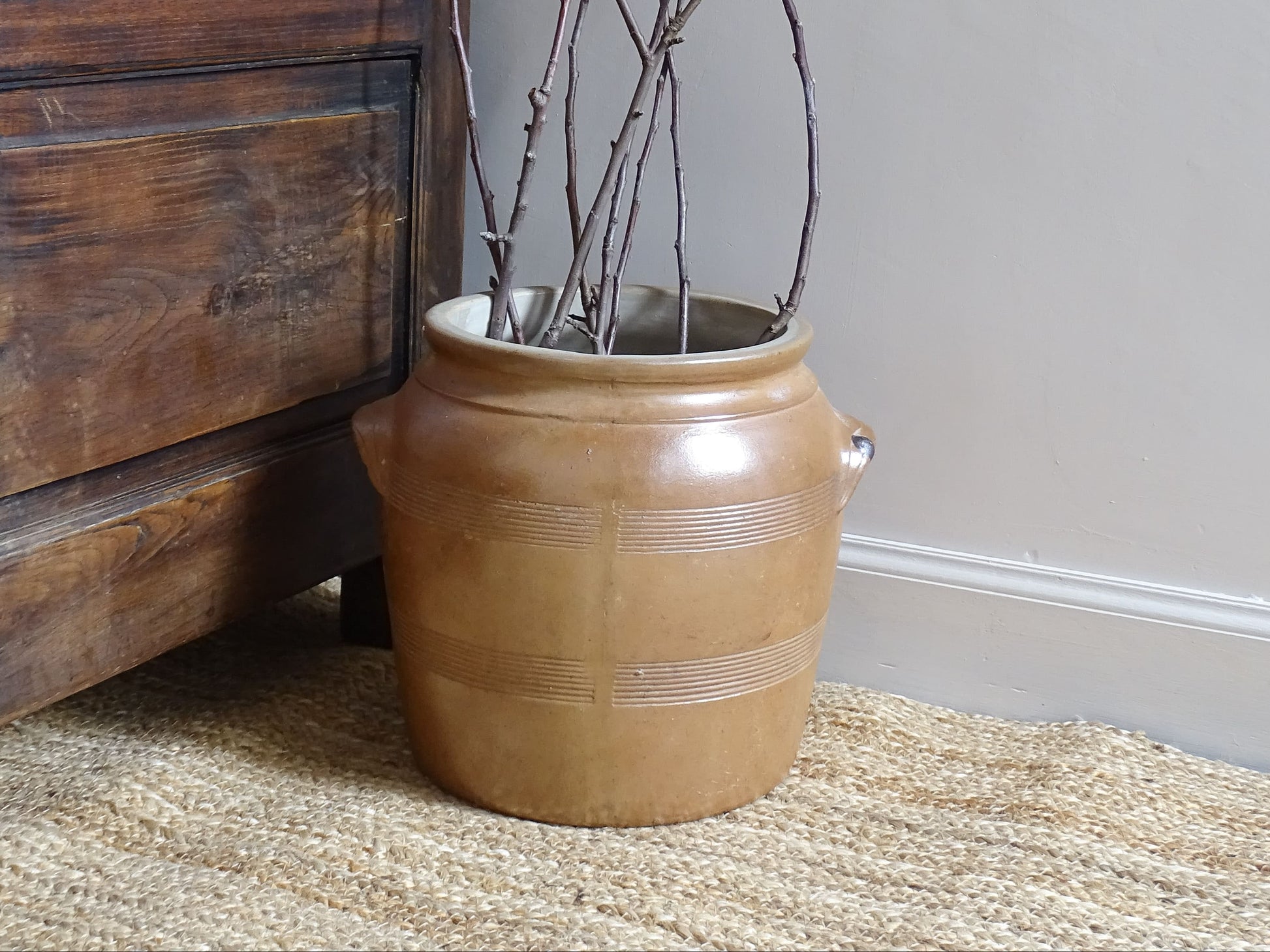 French antique stoneware cache pot or confit jar with a brown glaze, filled with branches.