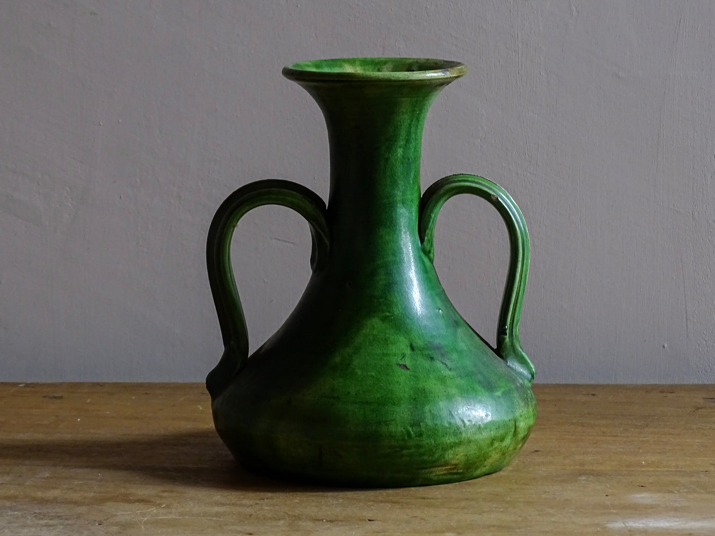 French antique art nouveau pottery vase with a green glaze in a deep tone with splashes of soft yellow. Organic in shape, this twin handled antique vase has an elongated neck