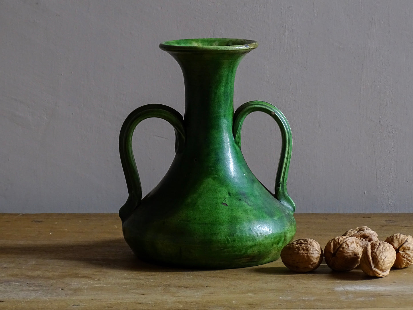 French antique art nouveau pottery vase with a green glaze in a deep tone with splashes of soft yellow. Organic in shape, this twin handled antique vase has an elongated neck