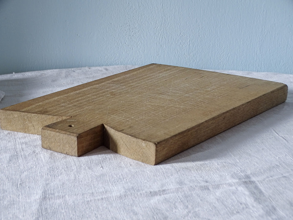 Close-up angled view of vintage French chopping board with distinctive squared handle, hanging hole and knife-marked wooden surface.