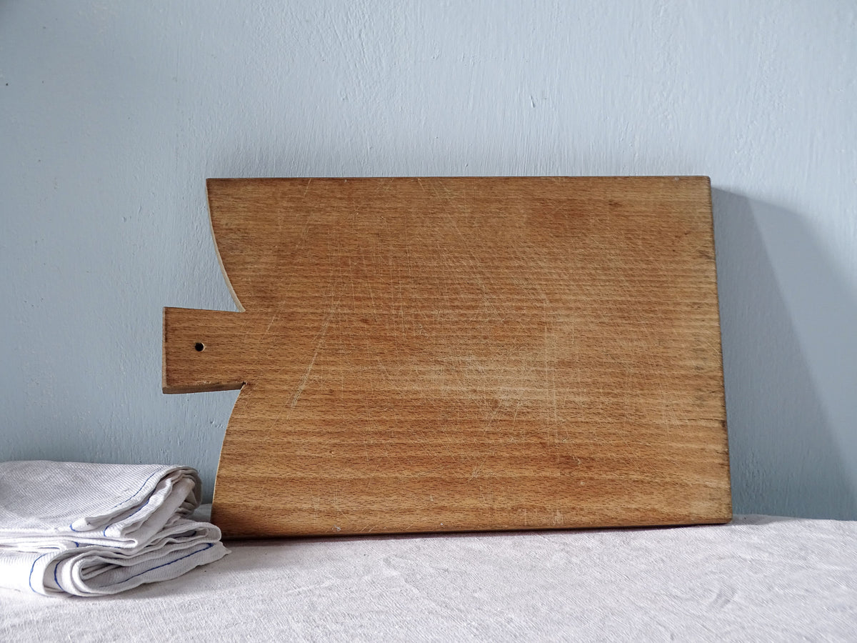 Opposite face of vintage French wooden cutting board showing its rectangular shape, short handle and naturally worn wood grain.